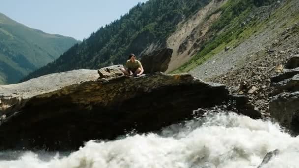 Turista hombre arroja piedras en un río de montaña, disfrutando de la vista — Vídeo de stock