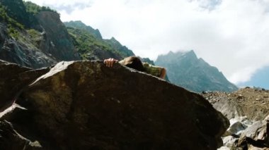 Mutlu bir adam bir kaya tırmanıyor ve ellerini yukarı yükseltir. Bouldering dağlarda