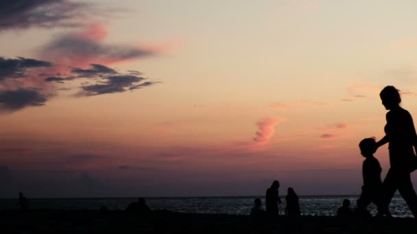 Silhouette di una madre di famiglia con una passeggiata per bambini sullo sfondo del mare al tramonto — Video Stock