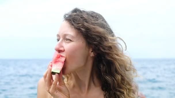 Retrato de uma mulher mordendo uma fatia de melancia no mar câmera lenta — Vídeo de Stock