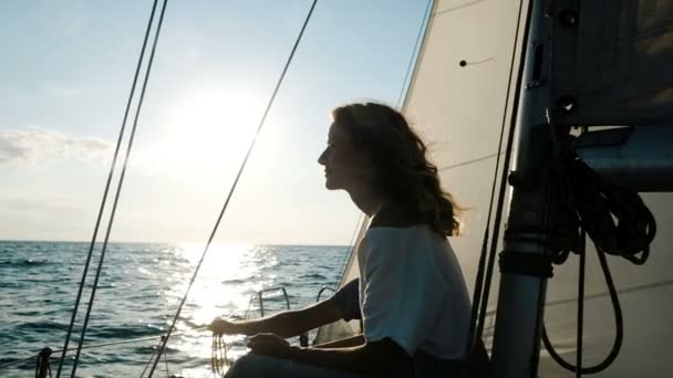 Szczęśliwa młoda kobieta w sukni siedzi na pokładzie w pobliżu maszt z żaglem o zachodzie słońca — Wideo stockowe