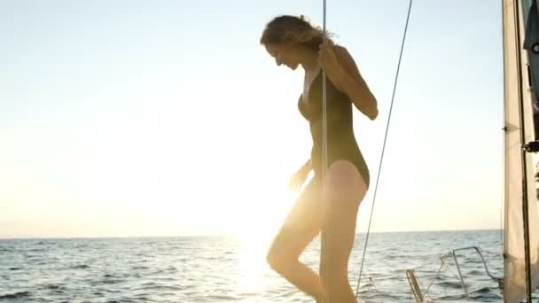 Slim κοπέλα ετοιμάζεται να πηδήσει από ένα ιστιοπλοϊκό σκάφος στα ανοικτά της θάλασσας σε ηλιοβασίλεμα — Αρχείο Βίντεο