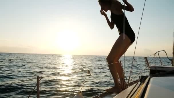 Smukłe piękne dziewczyna skacze od jachtu do otwartego morza na zachód, zwolnionym tempie — Wideo stockowe
