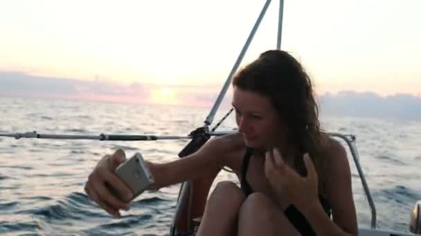 Jonge vrouw zeilen jacht en maakt gebruik van een smartphone - werpt een selfie — Stockvideo