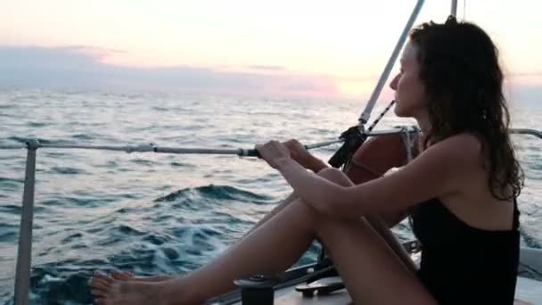 Mujer en traje de baño se sienta en la popa de un yate y disfruta de vistas al mar al atardecer — Vídeos de Stock