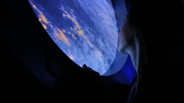 Девушка смотрит в иллюминатор в космосе — стоковое видео
