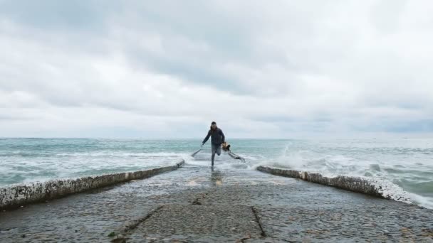 El hombre huye de las grandes olas en el muelle, el tipo entra en el agua y se ríe, en cámara lenta — Vídeo de stock