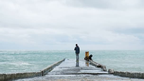 Чоловік стоїть на краю пірсу в штормі на морі, хвилі б'ються проти пірсу, повільний рух — стокове відео