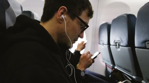 ชายคนหนึ่งฟังเพลงบนหูฟังและใช้โทรศัพท์ในเครื่องบิน — วีดีโอสต็อก