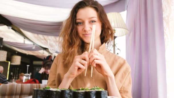 Hermosa chica caucásica rompe palos y come rollos en un restaurante japonés — Vídeo de stock