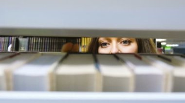 Kız bookshelf kapalı kitap alır ve geri koyar görünümü ile raflar