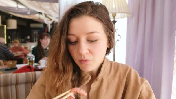 Joven hermosa chica con ojos azules comiendo pescado crudo con palillos en un restaurante — Vídeo de stock