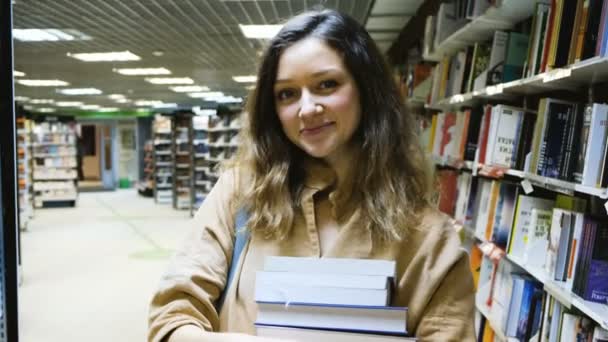 Bella ragazza tiene un mucchio di libri e mostra un pollice in alto in biblioteca — Video Stock