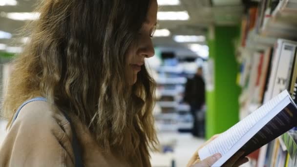 Mooi jong meisje bladeren door een boek in een boekhandel — Stockvideo