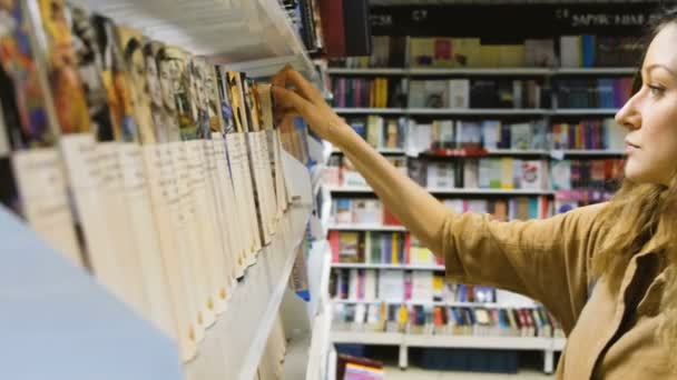 Uma jovem escolhe um livro em uma livraria — Vídeo de Stock