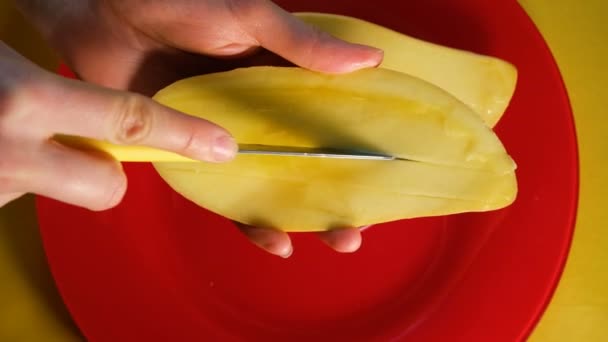 Девушка режет спелый тайский манго с ножом на ломтиках на красной пластинке и желтом фоне, вид сверху — стоковое видео