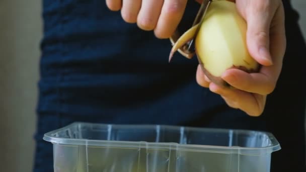 Mujer chef pelando patatas con cortador de verduras sobre contenedor de plástico de cerca — Vídeo de stock