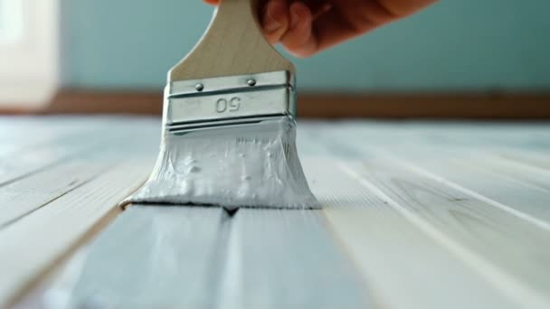 Pintor conduce su pincel a lo largo de una tabla de madera con pintura blanca en cámara lenta. Enfoque selectivo, primer plano — Vídeos de Stock