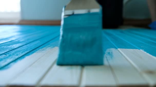 Pintor conduce su pincel a lo largo de una tabla de madera con pintura azul en cámara lenta, vista superior — Vídeos de Stock