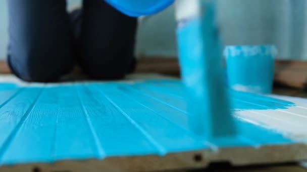 Pittore guida il suo pennello lungo una tavola di legno con vernice turchese al rallentatore, vista dall'alto — Video Stock
