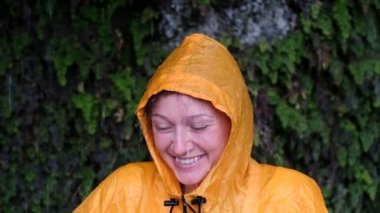 Yağan yağmur altında ağır çekim sarı yağmurluk içinde gülümseyen kadın portresi