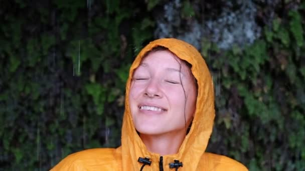 Πορτρέτο του ένα μπλε-eyed κορίτσι σε μια κίτρινη βροχή παλτό σηκώνει κεφάλι, κλείνει τα μάτια και χαμόγελα — Αρχείο Βίντεο