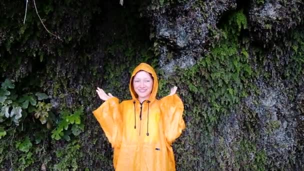 Νεαρή γυναίκα σε μια κίτρινη βροχή παλτό στέκεται, σηκώνει το κεφάλι και τα χέρια σε αργή κίνηση — Αρχείο Βίντεο