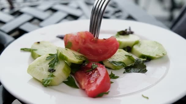 Вилка пронзает салат из помидоров и огурцов на белой тарелке крупным планом, замедленным движением — стоковое видео