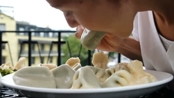 Молодая женщина берет и ест хинкали над тарелкой руками в ресторане — стоковое видео