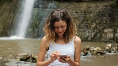 Kadın arka planda büyük bir şelale, Internet bağımlılığı doğada bir akıllı telefon kullanır