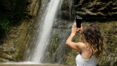 Kız telefonunu dalgalar, görüntülü arama tarafından konuşuyor ve bir şelale gösterir mutlu gülümseyerek, telefonda gülümsüyor
