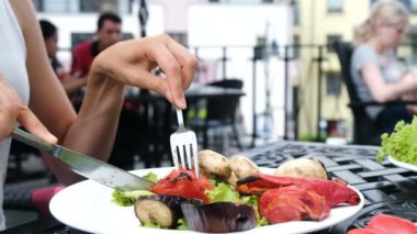 Kadın kavrulmuş domates bir bıçakla keser, kız bir ızgara sebze bir çatal ile beslenir.