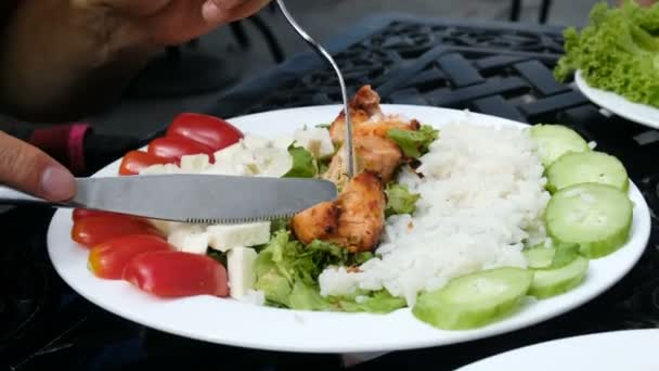 Человек режет кусок жареной курицы и ест вилкой с тарелки с салатом крупным планом — стоковое видео