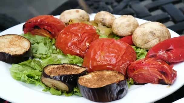 Mulher leva um garfo de tomate assado em um prato com legumes grelhados de perto — Vídeo de Stock