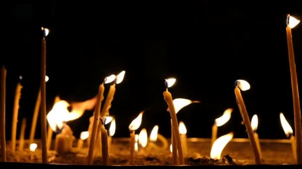 Воскові свічки горять у темряві в церкві на темному фоні, повільний рух — стокове відео