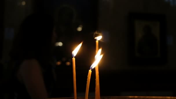 Quatro velas queimando na igreja no escuro contra o fundo das pessoas, câmera lenta — Vídeo de Stock