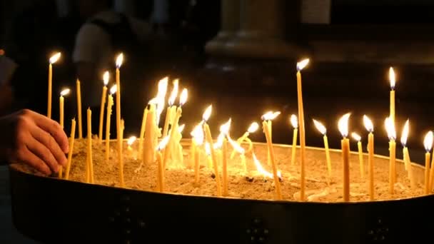 Girl puts a candle burning in the church in the dark against the backdrop of people. Sand Candlestick — Stock Video