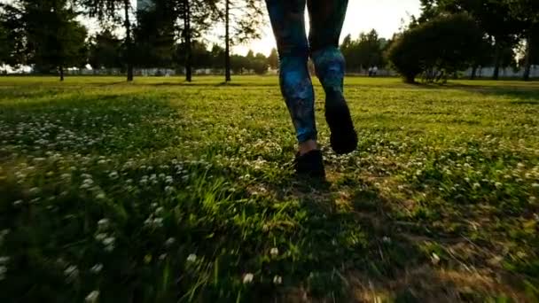Спортивные женские ноги в колготках и кроссовках бегают по траве на закате — стоковое видео