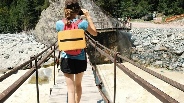 Mujer joven caminando a través del puente de madera sobre el río de montaña — Foto de Stock