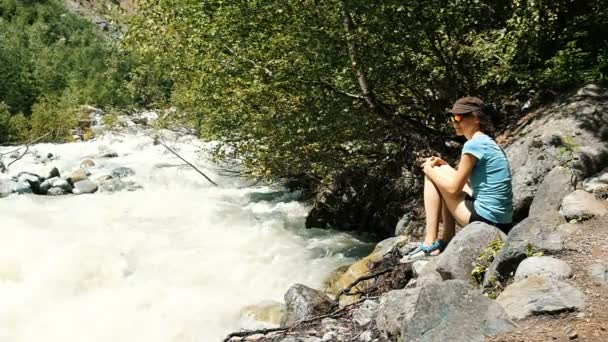 Žena sedí na kameni a dívá na vířící proudy horské řeky, pobíhající po lese, pomalý pohyb — Stock video