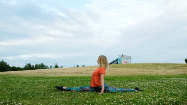 Художественная гимнастка сидит на продольном и поперечном расщеплении в городском парке, гибкая растяжка — стоковое видео