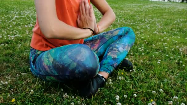 Mujer medita y haciendo yoga dobla sus manos en namaste sentado en la posición de loto de cerca sobre la hierba en un parque de la ciudad en la naturaleza — Vídeo de stock