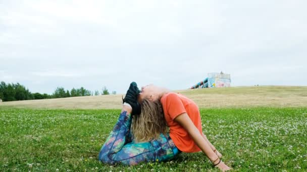 Женщина растягивает спину и делает изгибы, лежащие на траве, девушка тренируется в городском парке в природе — стоковое видео