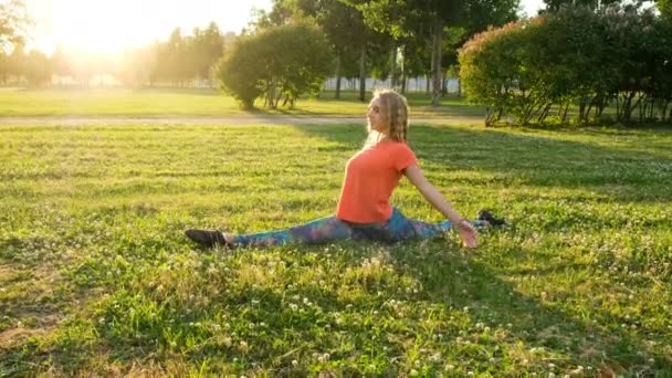 La gimnasta artística se sienta en las divisiones longitudinales y transversales. Estiramiento en el parque de la ciudad — Vídeo de stock