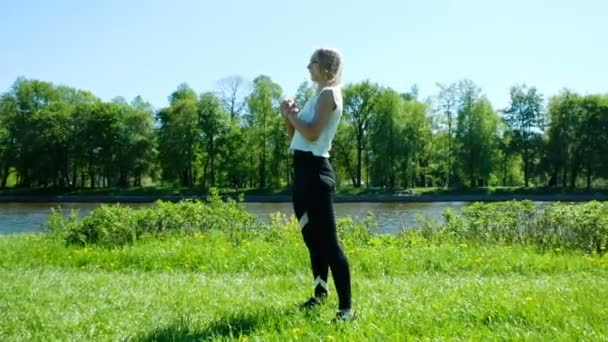 Menina desportiva mantém o aquecimento na natureza saltos e bombas pernas músculos, câmera lenta — Vídeo de Stock