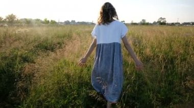 Woman walks across the field and hand touches high grass at sunset, slow motion