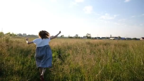 Vrouw in jurk loopt grappig weg in een veld in een veld bij zonsondergang, Slowmotion en camerabewegingen — Stockvideo