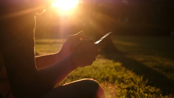 Ο άνθρωπος χρησιμοποιεί ένα smartphone στο πάρκο στο ηλιοβασίλεμα το καλοκαίρι, τεχνολογία αναψυχής έννοια — Αρχείο Βίντεο