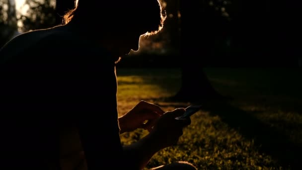 Hermosa silueta de un hombre con un teléfono inteligente en sus manos al atardecer. Relájate, concepto de naturaleza . — Vídeo de stock