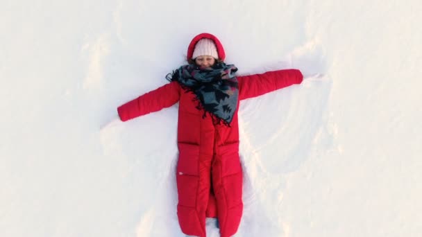 Caméra aérienne se déplace de femme couchée dans la neige et faire ange de la neige — Video